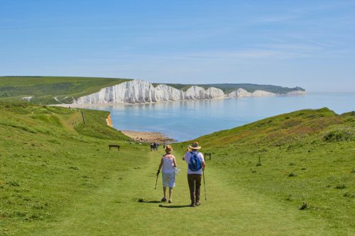 An older couple walking down a grassy hill towards a body of water surrounded by white cliffs.