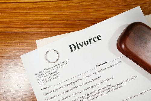 A brown wood table with white divorce papers and a gold wedding band